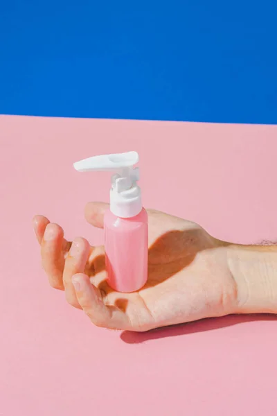Cosmetic cream for face blank bottle in hand. Bio organic product on pink and blue background. minimal beauty and spa pop art concept.