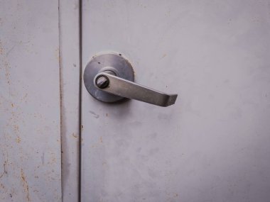 Close-up of a stainless steel lever handle mounted on a metal door with visible scratches and rust stains. Ideal for industrial design, architecture, or maintenance themes.