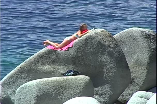 Chica toma el sol en la roca mientras lee un libro — Vídeos de Stock