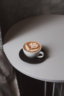 Düz beyaz kahve, beyaz masada çiçek latte sanatı, hippi kahve dükkanı konsepti. Minimalist arka plan, kopyalama alanı. Yukarıdan