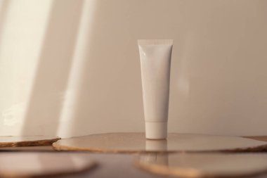 Beyaz kozmetik tüp sıcak yumuşak ışık arka planında. Minimalizm ürünü hala hayat. Işık ve gölge. Güzellik blogu, cilt bakımı. Boşluğu kopyala