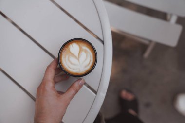 Kahve dükkanında kapuçino içen bir kadın. Yiyecek içecek fotoğrafçılığı konsepti. Lezzetli, atmosferik karamsar bir çekim. Kapat, üst görünüm