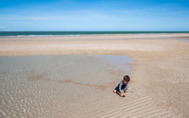 Tatlı çocuk yazın kumlu sahilde eğleniyor.