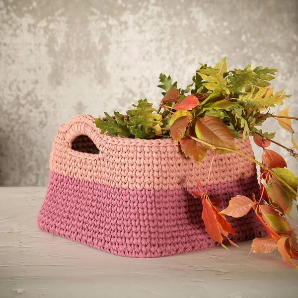 a knitted basket with autumn leaves is on the table