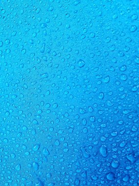 Kumaşın üzerindeki su damlacıkları. Mavi arka plan mavi lifli su geçirmez kumaş üzerinde yağmur damlaları gösteriyor. Damlacıklar farklı boyutlarda, canlandırıcı bir soyut desen oluşturuyor..