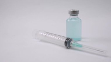 Steril tıbbi şırınga ve aşı şişesi beyaz bir zemine yerleştirilmiş.
