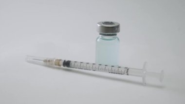 Tıbbi şırınga ve sıvı ilaç şişesi temiz beyaz bir arka planda dönen bir masaya yerleştirilmiş. Tıbbi Şırınga ve Aşı Şişesi