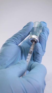Eldivenli bir doktor tarafından mavi aşı sıvısıyla doldurulan bir şırınganın detaylı makro çekimi. Sağlık ve tıbbi kavramlar