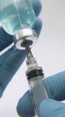 Şırıngayı mavi aşı sıvısıyla dolduran eldivenli bir tıp uzmanının makro yakın çekimi klinik hassasiyeti ve modern sağlık prosedürlerini vurguluyor..