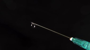 Siyah arka plana sıvı damlatan şırınga ucu tıbbi hassasiyet, aşı temaları ve sağlık konseptlerini vurguluyor..
