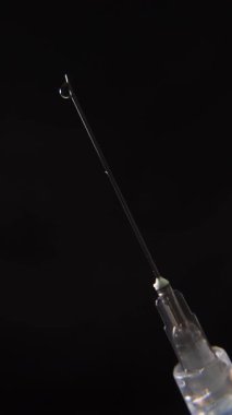 Siyah arka planda bir damlacık oluşturan bir şırınga iğnesi.