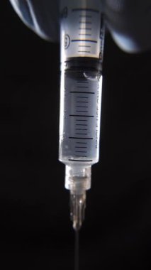 Bir şırınganın içindeki sıvı tıbbı, tamamen dolu bir şırıngayla siyah bir zemin üzerinde yakın çekim yap..