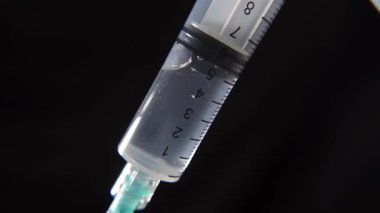 Siyah zemin üzerinde bir şırınga içinde tıbbi sıvının yakın plan çekimi, klinik tedavi ve ilaç prosedürlerini göstermek için iğnenin sıvıyı enjekte etmesi