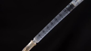 Sıvı ilaç içeren tam dolu bir şırınganın makro görünümü, iğne yapılırken koyu bir arka planda gösterilir.