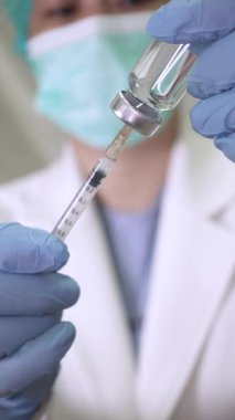 Koruyucu eldivenli bir doktor tarafından ilaçla doldurulan şırınganın detaylı görüntüsü aşı ve tıbbi bakımı sembolize ediyor..