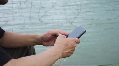 Bir gölün kenarında akıllı bir telefonu tutarak ellerinizi kapatın, doğal ve huzurlu bir ortamda günlük kullanım teknolojisini yakalayın.