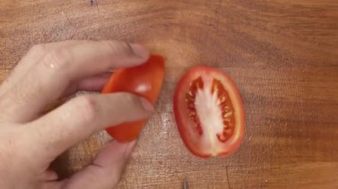 Tahta kesme tahtasının üzerinde keskin bir bıçakla olgun kırmızı domatesleri doğramak, pişirme ve sağlıklı yemekler için taze malzemeler hazırlamak.