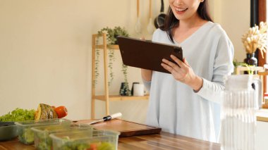 woman using digital tablet for recipe guidance while preparing healthy meals on kitchen counter..