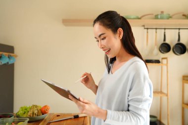 woman using digital tablet for recipe guidance while preparing healthy meals on kitchen counter..