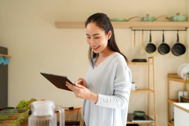 Woman organizing kitchen containers while using a tablet for meal planning on counter..