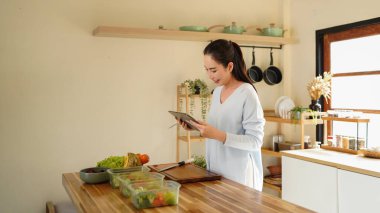 woman using digital tablet for recipe guidance while preparing healthy meals on kitchen counter..