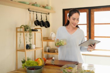 woman using digital tablet for recipe guidance while preparing healthy meals on kitchen counter..
