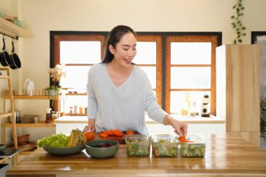 A woman preparing healthy meal prep in a bright kitchen with fresh vegetables and fruits.