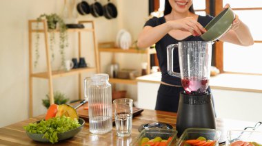 A woman adds fresh blueberries to a blender. Fresh berry smoothie preparation, Woman, hands or blender with blueberries or fruit for smoothie or healthy diet in home..