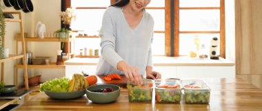 A woman preparing healthy meal prep in a bright kitchen with fresh vegetables and fruits.