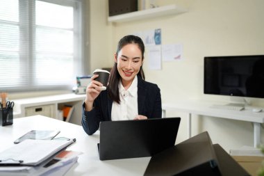 businesswoman drinking coffee while using laptop in office.