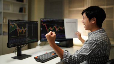 business man congratulations stock trader sitting at a desk in front of computer monitors.