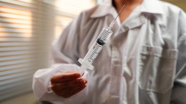 Woman doctor wearing uniform holding syringe in clinic.