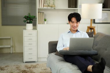 Dizüstü bilgisayarla çalışan serbest çalışan bir adam evdeki koltukta oturuyor, internette sörf yapıyor, modern teknolojiler kullanıyor, serbest alan kullanıyor..