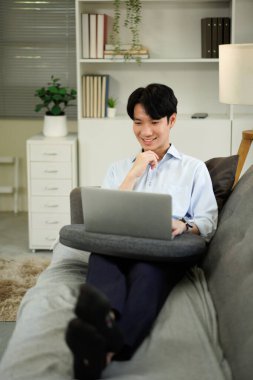 Dizüstü bilgisayarla çalışan serbest çalışan bir adam evdeki koltukta oturuyor, internette sörf yapıyor, modern teknolojiler kullanıyor, serbest alan kullanıyor..