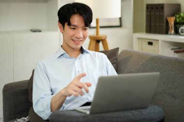 Dizüstü bilgisayarla çalışan serbest çalışan bir adam evdeki koltukta oturuyor, internette sörf yapıyor, modern teknolojiler kullanıyor, serbest alan kullanıyor..