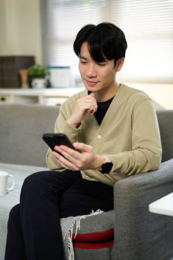 Akıllı telefon tutan ve oturma odasındaki bir kanepede otururken daktilo yazan bir adama yakın çekim, iş, iletişim ve teknoloji konsepti..