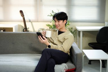 Rahat adam kanepede kahve, telefon, rahat ofis titreşimleri. Doğal Işıklı Sıradan Oturma Odası Sahnesi.