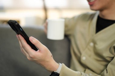 Rahat adam kanepede kahve, telefon, rahat ofis titreşimleri. Doğal Işıklı Sıradan Oturma Odası Sahnesi.