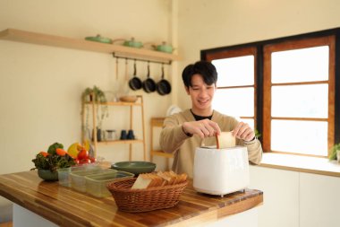 Genç Asyalı adam sabah mutfakta sandviçler için çıtır çıtır tost yapıyor..