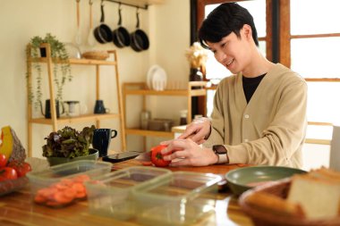 Bir adam mutfakta domates kesiyor. Gülümsüyor ve süreçten zevk alıyor gibi görünüyor.