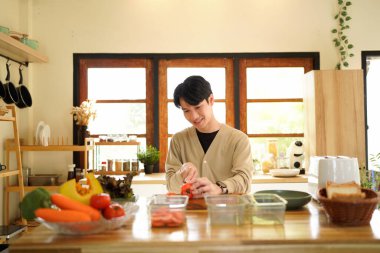 Bir adam mutfakta domates kesiyor. Gülümsüyor ve süreçten zevk alıyor gibi görünüyor..