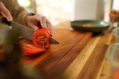 Adam ahşap kesme tahtasıyla mutfak bıçağıyla taze domates kesiyor...