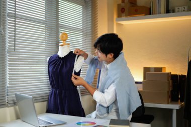 Şık giyimli bir erkek tasarımcı yeni bir kıyafet koleksiyonu yaratıyor, ölçüm bandıyla kıyafet parametrelerini ölçüyor ve stüdyoda dururken bunları kağıda döküyor...