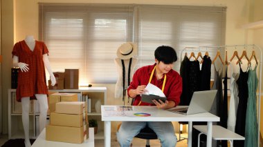 Erkek terzi eskizlerle tasarım üzerinde çalışır, materyalleri ve özel yapım boyutları incelemek için dizüstü bilgisayar kullanır. Erkek profesyonel terzi atölyede lüks kıyafetler yapıyor..