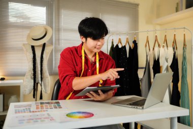 Erkek terzi eskizlerle tasarım üzerinde çalışır, materyalleri ve özel yapım boyutları incelemek için dizüstü bilgisayar kullanır. Erkek profesyonel terzi atölyede lüks kıyafetler yapıyor..