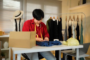 Odaklanmış bir erkek terzi iyi donanımlı bir stüdyoda mavi kumaşı inceliyor. Dikiş aletleri, hassasiyet ve beceri sergiliyor. online giyim mağazası.