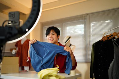 Asyalı adam internet üzerinden akıllı telefon canlı yayınıyla kıyafet ve aksesuar satıyor, evde internet üzerinden ticaret yapıyor..