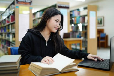 Genç üniversiteli kadın kütüphanede tek başına çalışırken bilgisayarında çalışıyor...