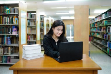 Genç üniversiteli kadın kütüphanede tek başına çalışırken bilgisayarında çalışıyor...