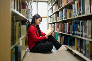 Okul, üniversite veya üniversite kampüsünde eğitim, öğrenim ve araştırma için kütüphanede kitap okuyan Asyalı genç kadın..